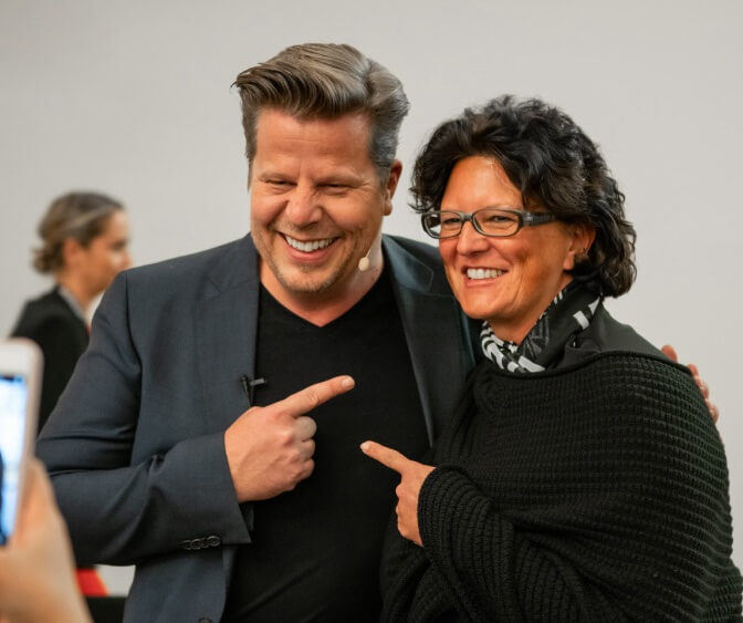 Alex Fischer und eine Workshop-Teilnehmerin lachen und zeigen gegenseitige Wertschätzung. Dieses Bild zeigt die menschliche Seite seiner Arbeit und seinen nahbaren Umgang mit seinen Zuhörern und Lesern.